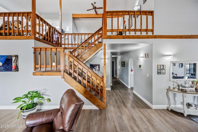 staircase with baseboards, a high ceiling, ceiling fan, arched walkways, and wood finished floors
