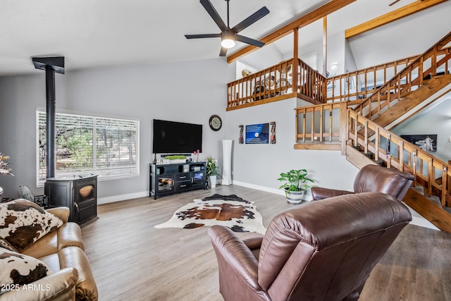 living room featuring wood finished floors, a wood stove, baseboards, and stairway