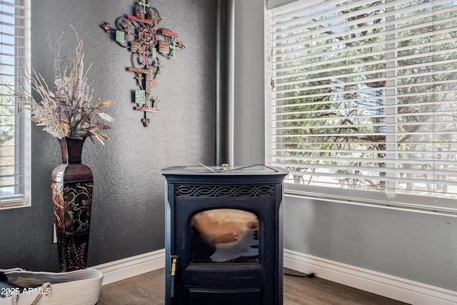 interior details featuring wood finished floors, a wood stove, baseboards, and a textured wall