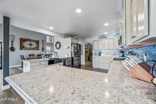 kitchen featuring dark wood finished floors, dishwashing machine, a peninsula, arched walkways, and black refrigerator with ice dispenser