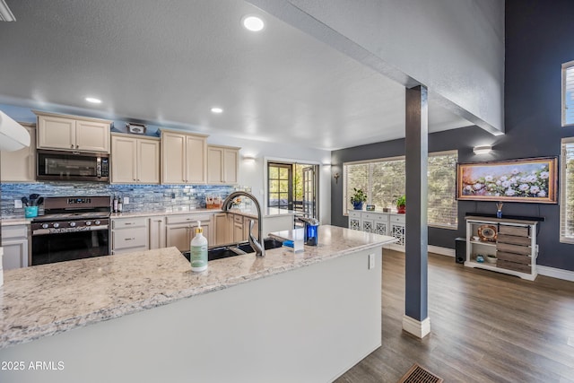 kitchen with tasteful backsplash, cream cabinetry, appliances with stainless steel finishes, a sink, and dark wood-style floors