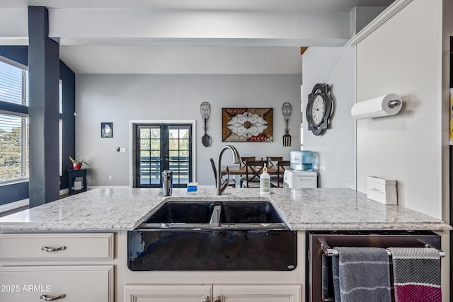 kitchen featuring french doors, white cabinetry, a sink, and light stone counters