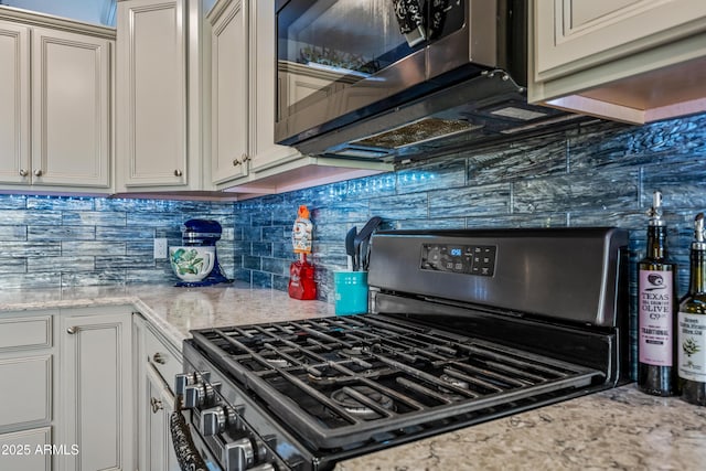 kitchen with tasteful backsplash, stainless steel gas stove, white cabinetry, and light stone countertops
