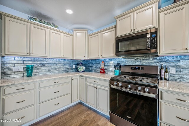 kitchen with light wood-style flooring, light stone counters, stainless steel appliances, cream cabinets, and backsplash