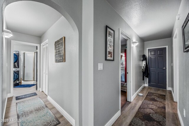 hallway with stacked washer and dryer, baseboards, arched walkways, and wood finished floors