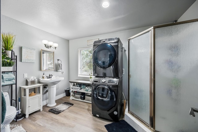 bathroom featuring baseboards, a sink, stacked washer and clothes dryer, wood finished floors, and a stall shower