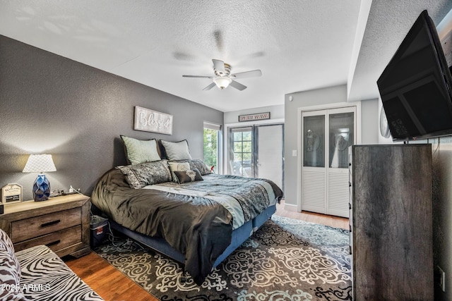 bedroom featuring a textured wall, a textured ceiling, a ceiling fan, access to exterior, and wood finished floors