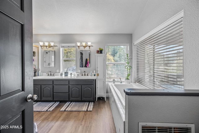 bathroom with an inviting chandelier, a bath, wood finished floors, a sink, and double vanity
