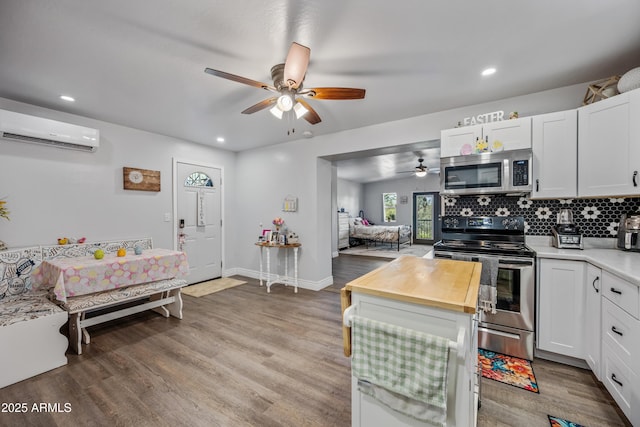 kitchen with butcher block counters, light wood-style floors, a wall unit AC, ceiling fan, and appliances with stainless steel finishes