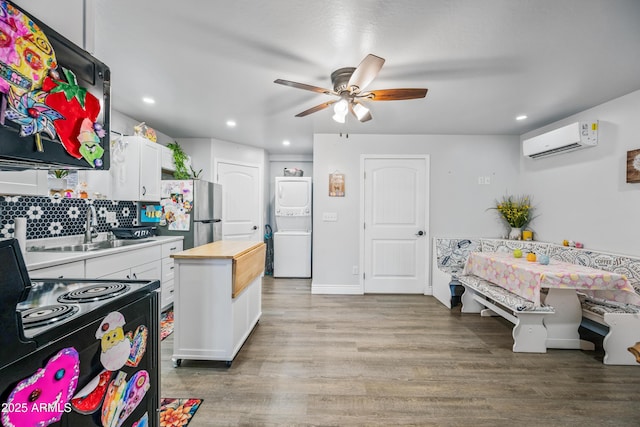 kitchen featuring ceiling fan, freestanding refrigerator, stacked washer / dryer, a sink, and an AC wall unit