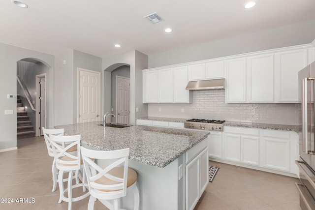 kitchen featuring a kitchen island with sink, stainless steel appliances, white cabinets, and light stone counters