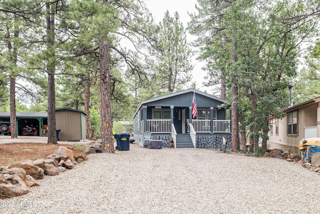 view of front of property with a storage unit, a porch, gravel driveway, and an outdoor structure