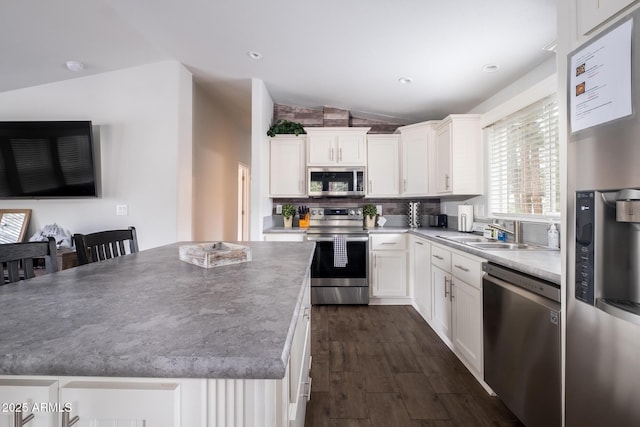 kitchen with dark wood-type flooring, a sink, a kitchen island, white cabinetry, and stainless steel appliances