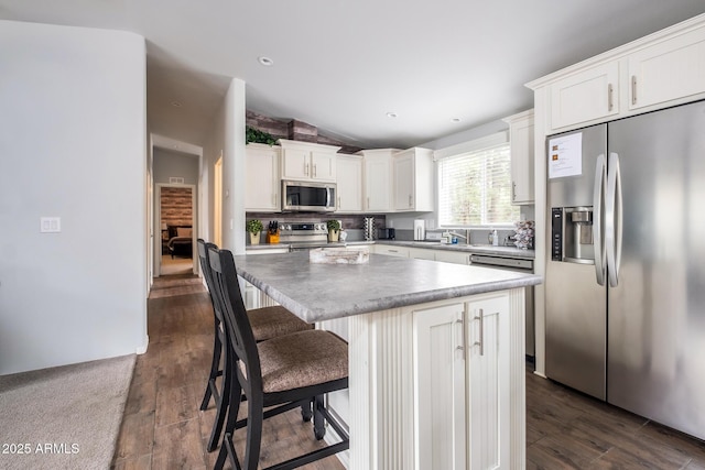 kitchen with a kitchen island, lofted ceiling, stainless steel appliances, dark wood-type flooring, and white cabinetry