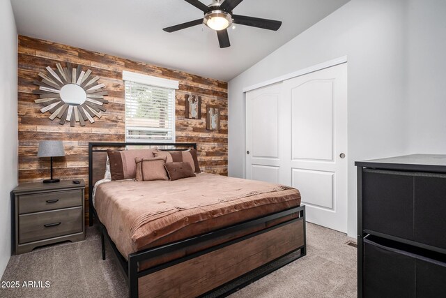 bedroom featuring a closet, wooden walls, light colored carpet, ceiling fan, and vaulted ceiling