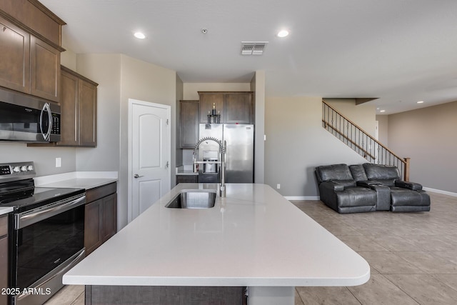 kitchen featuring an island with sink, a sink, open floor plan, stainless steel appliances, and light countertops