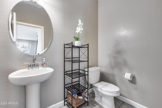 bathroom featuring baseboards, a sink, tile patterned floors, toilet, and a textured wall