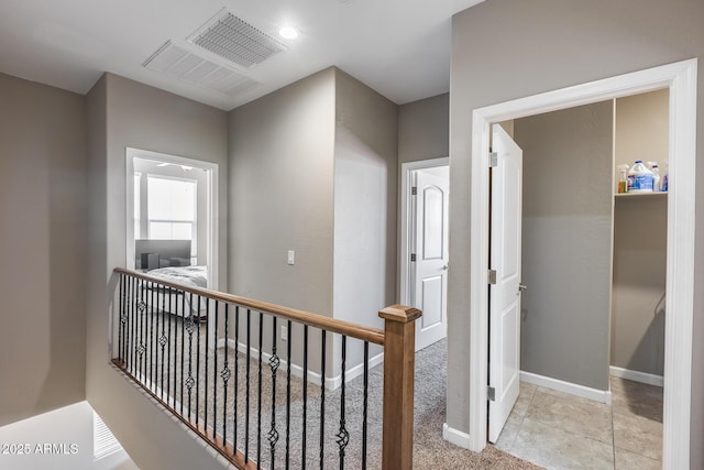 hallway with an upstairs landing, visible vents, light colored carpet, and baseboards