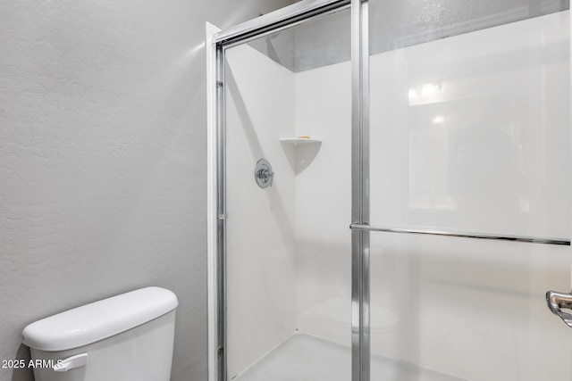 full bathroom featuring toilet, a shower stall, and a textured wall