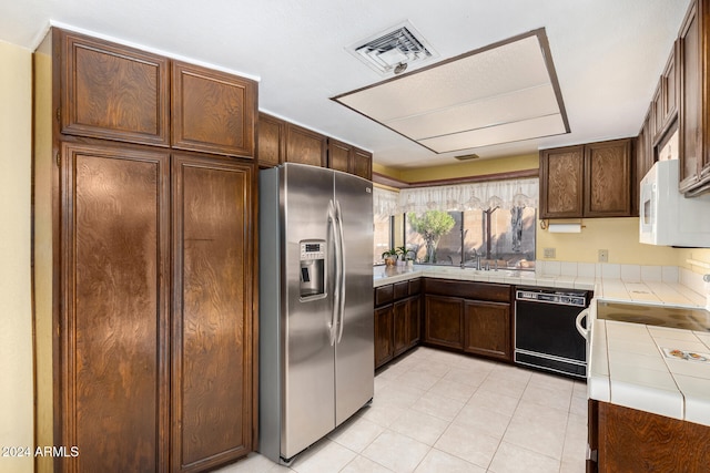 kitchen featuring tile counters, stainless steel fridge, light tile patterned floors, and black dishwasher