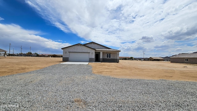 view of front of house with gravel driveway, an attached garage, and stucco siding