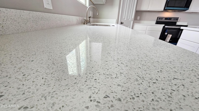 kitchen featuring a sink, electric range, white cabinetry, light stone counters, and speckled floor