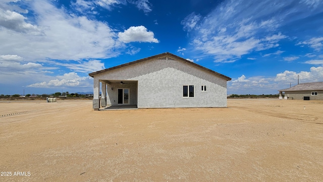 rear view of house featuring stucco siding and a ceiling fan