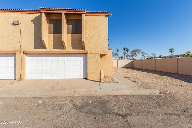 view of front facade featuring a garage, fence, concrete driveway, and stucco siding