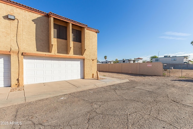 view of side of property with a garage, a tiled roof, fence, and stucco siding