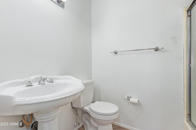 bathroom with baseboards, a shower with shower door, a sink, and toilet