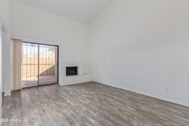 unfurnished living room featuring a fireplace with raised hearth, high vaulted ceiling, wood finished floors, and baseboards