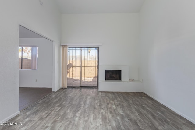 unfurnished living room featuring a fireplace with raised hearth, a high ceiling, wood finished floors, and baseboards