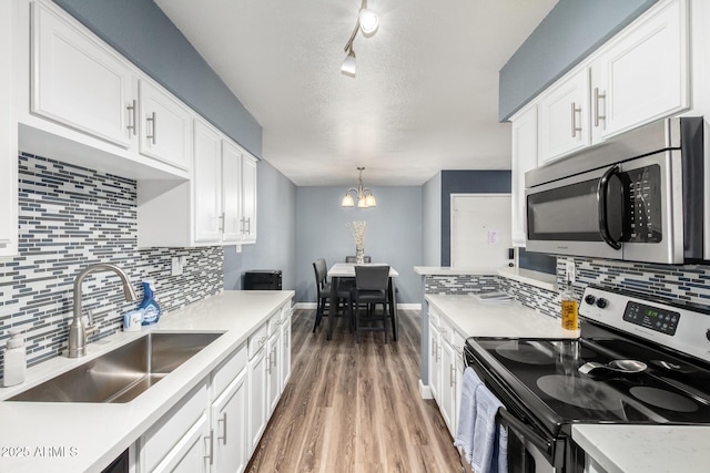 kitchen with a sink, white cabinets, light countertops, appliances with stainless steel finishes, and pendant lighting