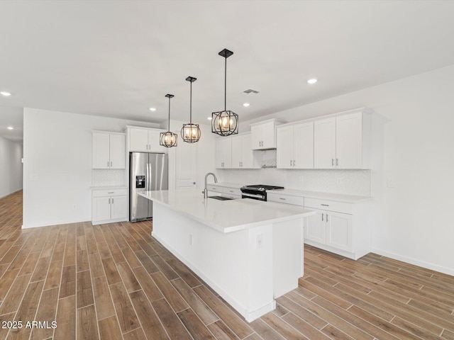 kitchen with stainless steel appliances, light wood finished floors, decorative backsplash, a sink, and a kitchen island with sink