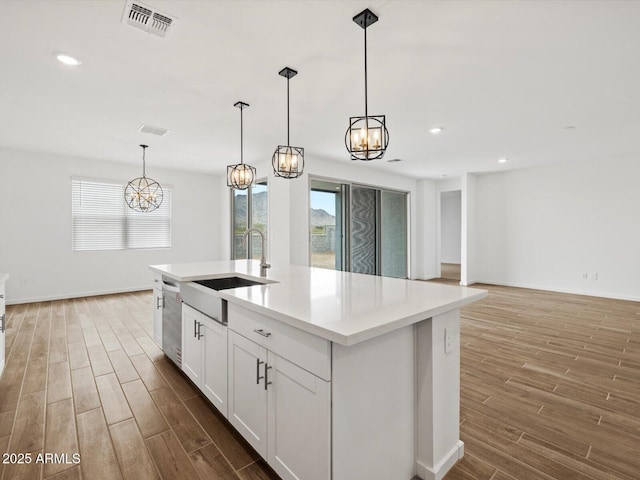 kitchen featuring a chandelier, a sink, wood finished floors, white cabinetry, and light countertops