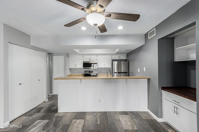 kitchen featuring dark hardwood / wood-style flooring, kitchen peninsula, a breakfast bar, white cabinets, and appliances with stainless steel finishes