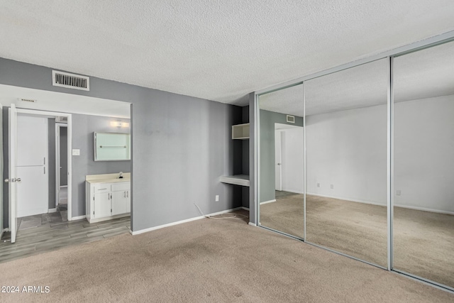 unfurnished bedroom with a textured ceiling, light colored carpet, and connected bathroom