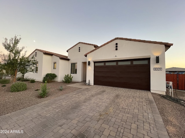 mediterranean / spanish-style house featuring a garage, decorative driveway, fence, and stucco siding