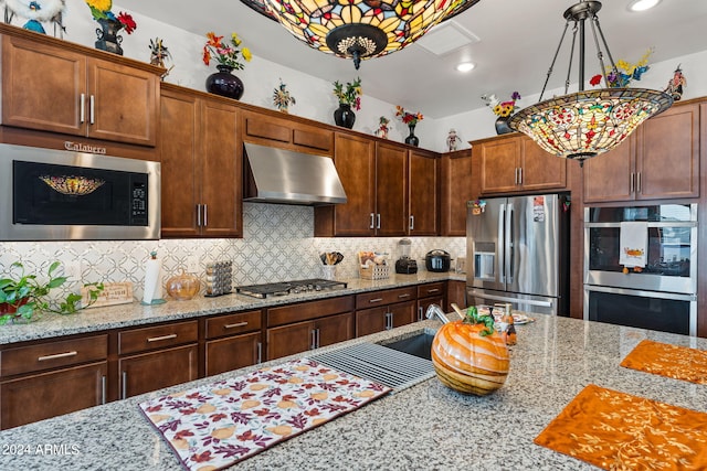 kitchen with under cabinet range hood, appliances with stainless steel finishes, decorative backsplash, and decorative light fixtures