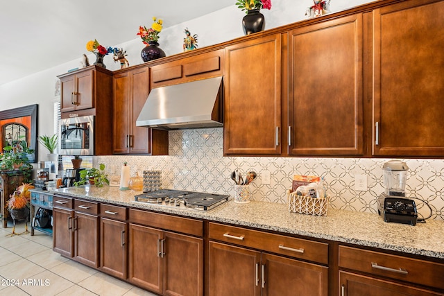 kitchen with light tile patterned floors, tasteful backsplash, appliances with stainless steel finishes, light stone countertops, and under cabinet range hood