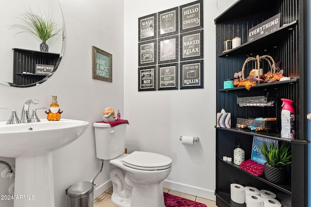 half bathroom featuring baseboards, a sink, toilet, and tile patterned floors