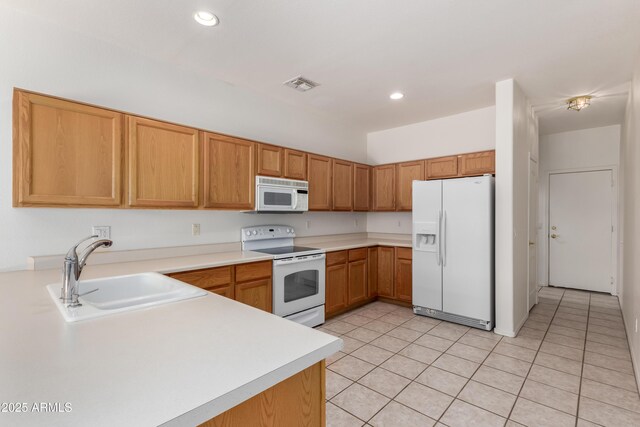 kitchen with light tile patterned floors, a peninsula, white appliances, and a sink