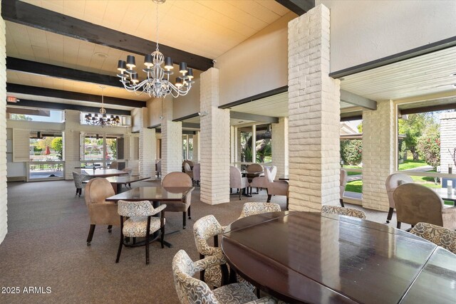 carpeted dining space featuring a notable chandelier, beamed ceiling, plenty of natural light, and decorative columns