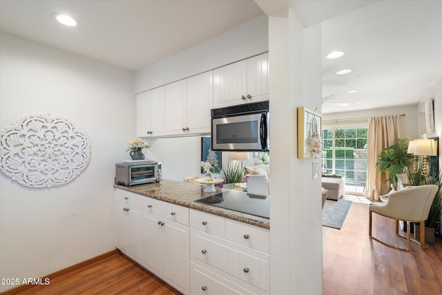 kitchen featuring stainless steel microwave, a toaster, wood finished floors, and white cabinetry