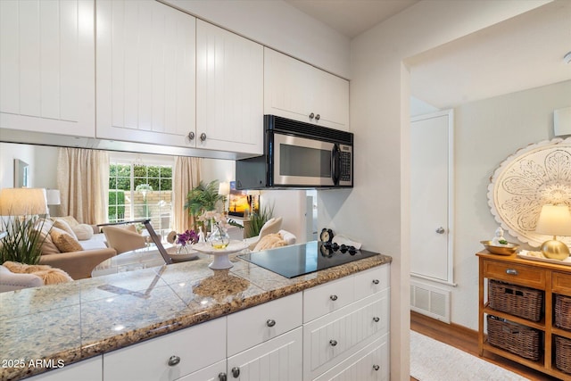 kitchen featuring visible vents, white cabinets, black electric stovetop, and wood finished floors