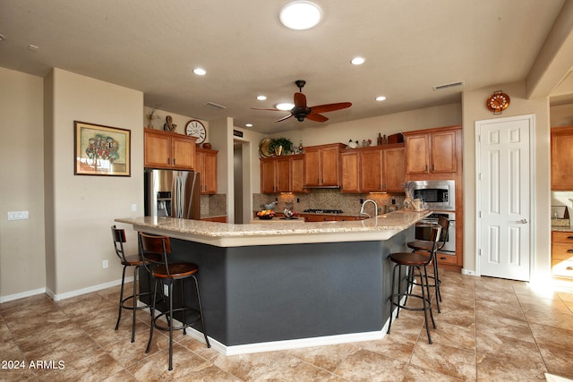 kitchen featuring tasteful backsplash, stainless steel appliances, a kitchen bar, and a large island with sink