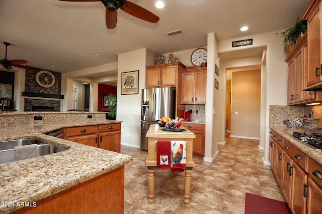 kitchen with decorative backsplash, a kitchen island, ceiling fan, stainless steel fridge with ice dispenser, and light stone countertops