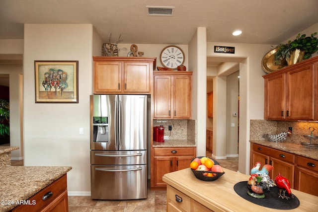 kitchen featuring stainless steel fridge with ice dispenser, light stone counters, and tasteful backsplash