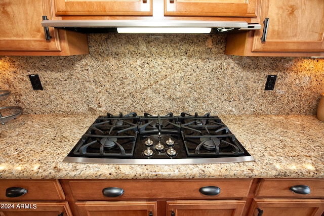 kitchen with light stone counters, decorative backsplash, stainless steel gas cooktop, and range hood