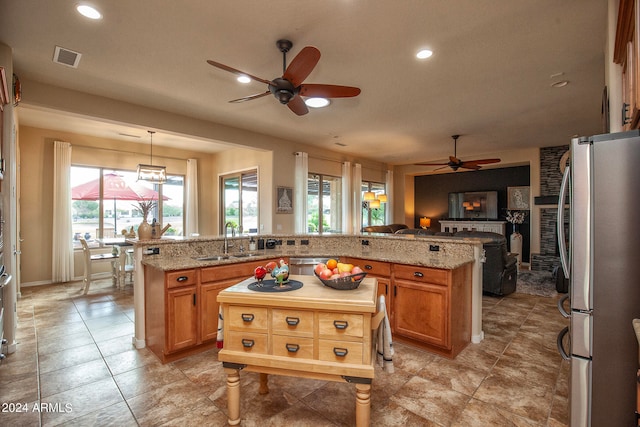 kitchen with a kitchen island, hanging light fixtures, stainless steel appliances, sink, and light stone countertops